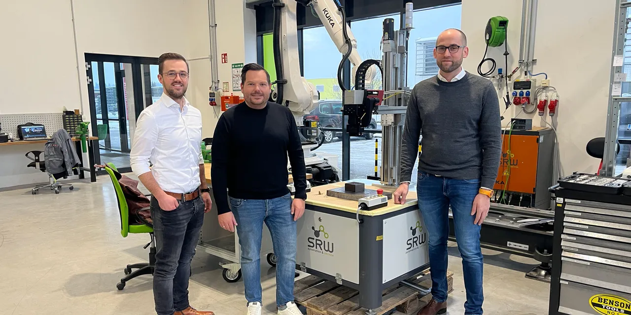 Drei Männer stehen vor einem industriellen SRW-Roboterarmsystem in einem modernen Lasertechnik-Arbeitsraum