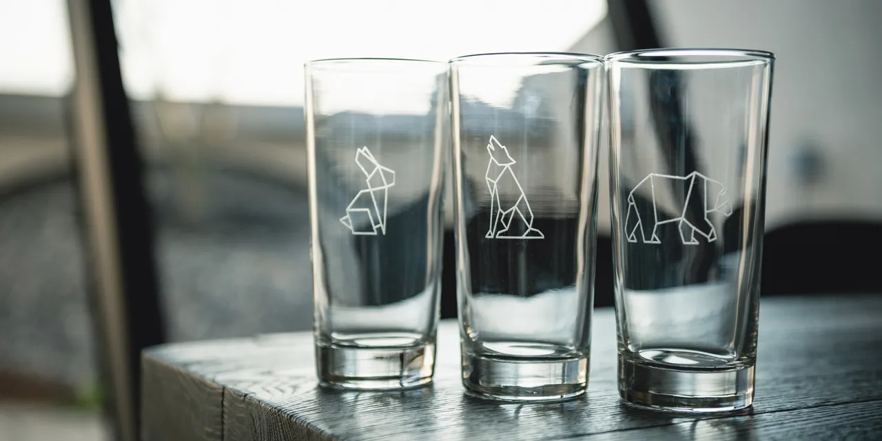 Coupes en verre avec des motifs d'animaux gravés à l'aide d'une machine gravure laser Trotec sur un plateau de travail en bois.