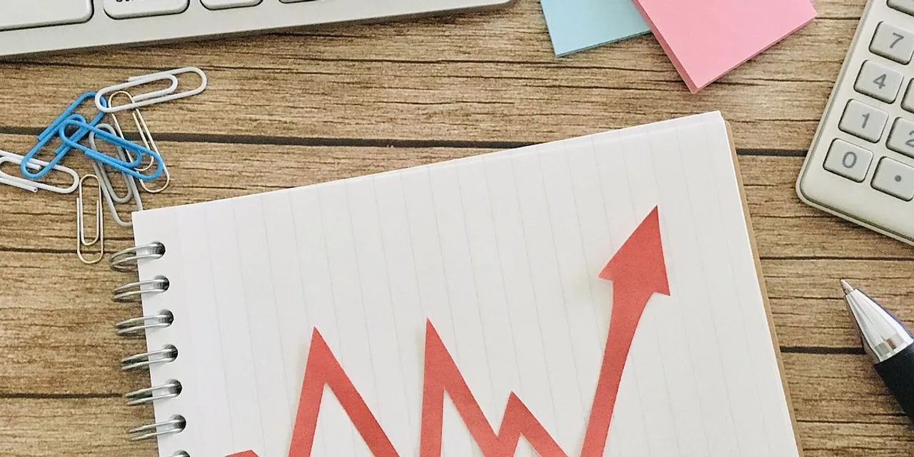 Red upward arrow on notebook page with calculator, pen, and paper clips on wooden desk
