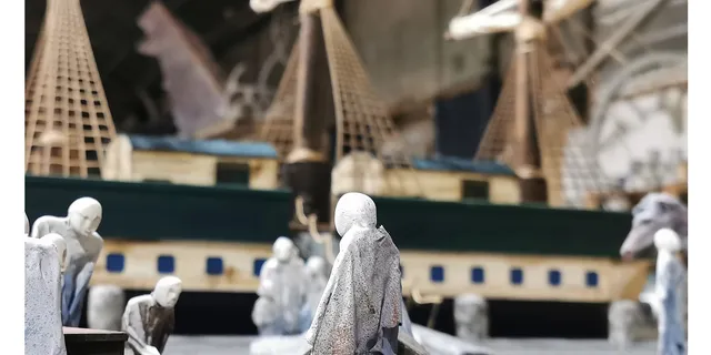 Miniature ship scene with detailed figures and sailing vessel in background