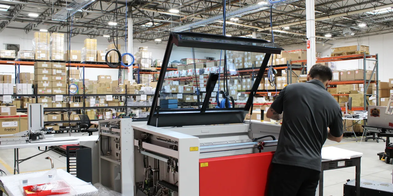 Technician assembling Trotec Speedy series CO₂ laser engraving machine in warehouse